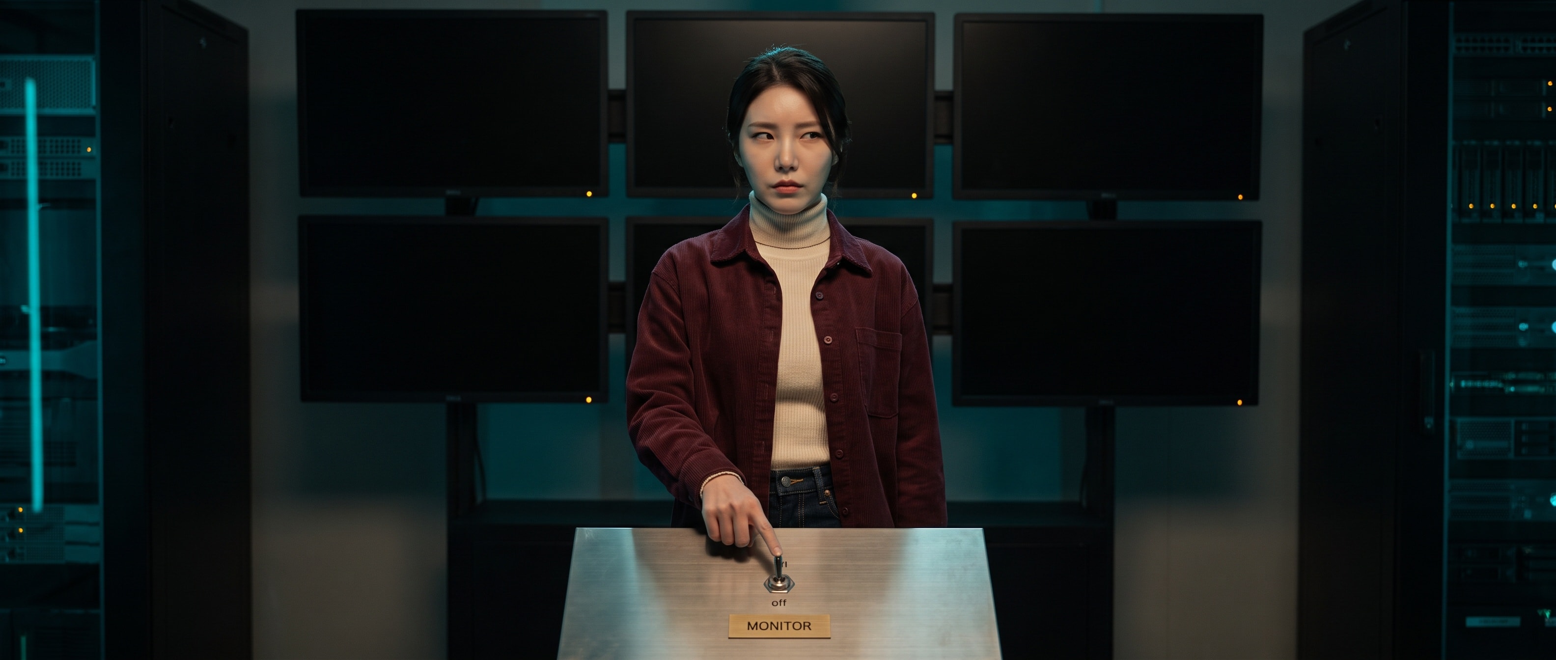 밤의 관제실 금속 스위치 패널 앞에 서서 MONITOR 라고 새겨진 명판 아래 내려간 토글에 손가락을 얹고 카메라를 곁눈질하는 루나, 뒤 벽면 모니터 여섯 대는 전부 꺼져 있다