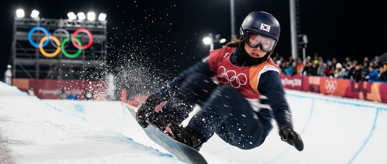 하프파이프 상공에서 회전하는 스노보더, 올림픽 조명 아래 눈 입자가 빛나는 순간